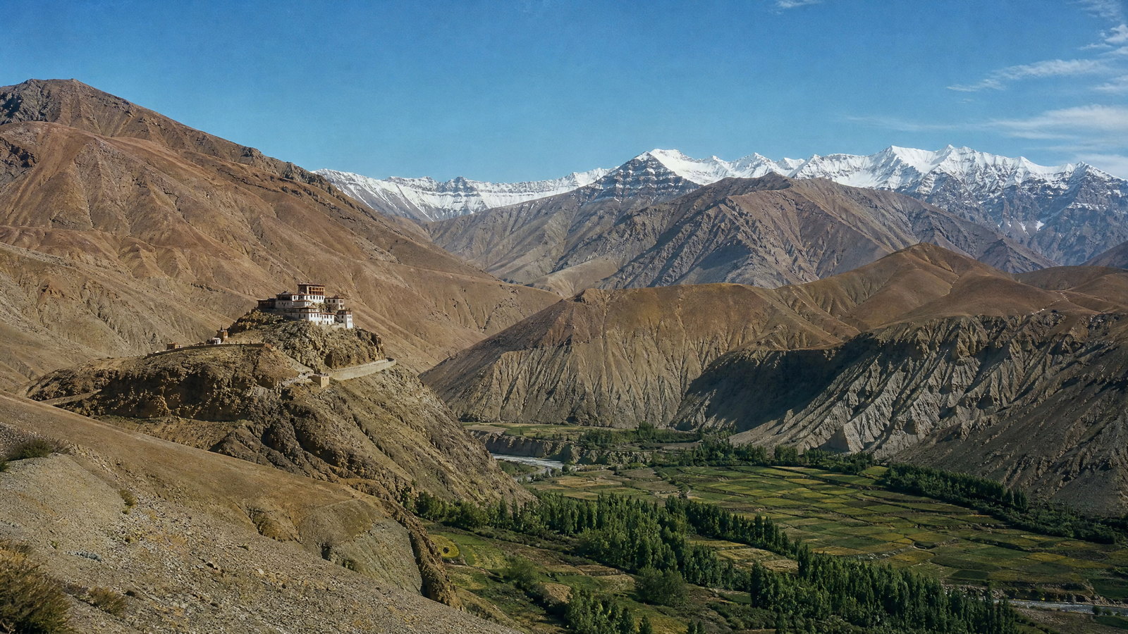 Early morning light across the upper Kinnaur valley, with slate-roofed houses, terraced fields and the snow-lined Kinner Kailash massif.