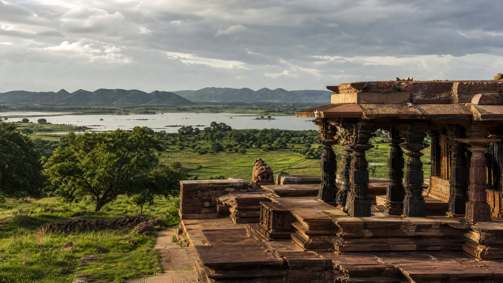 Ramappa Temple’s dark carved stone mandapa and stepped tower framed by quiet fields and low wooded hills in Telangana.
