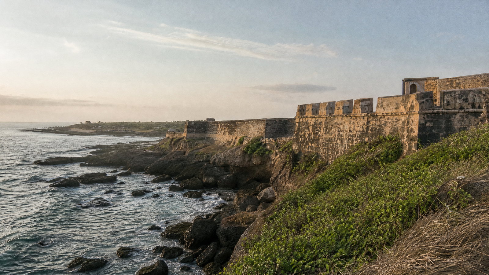Diu Fort’s weathered stone ramparts facing the Arabian Sea, with palms and an empty rocky shoreline.