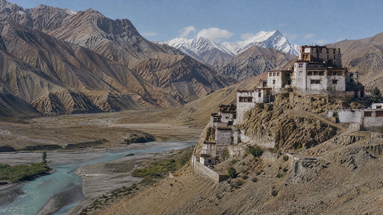 A still blue Pangong Tso framed by layered ochre mountains and a cloud-streaked high-altitude sky in eastern Ladakh.