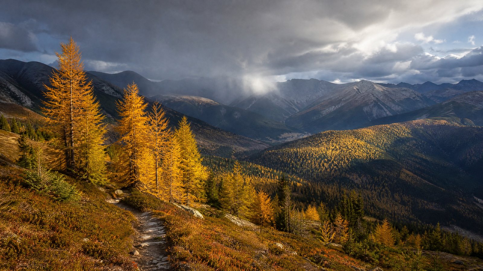 A lone hiker on an autumn mountain trail beneath clear sky and gathering cloud