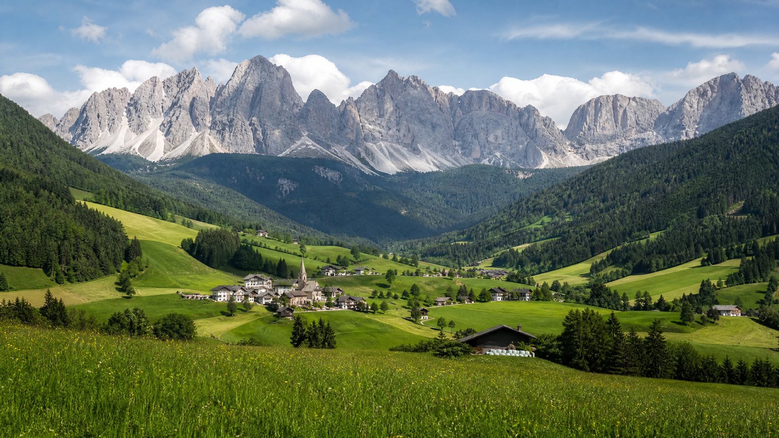 Green working valley and village beneath the pale peaks of the Dolomites