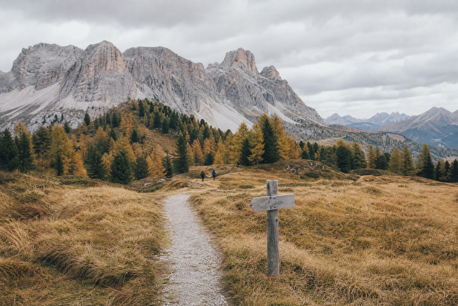 Two hikers on an autumn trail beneath pale Dolomites peaks