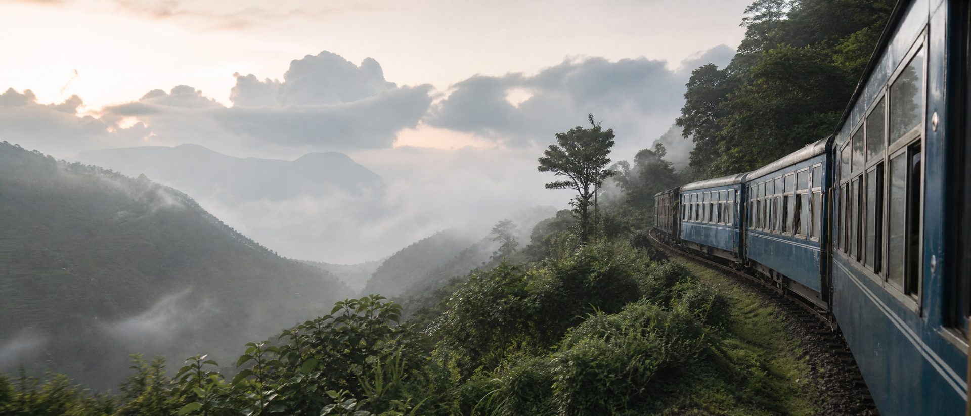 A blue heritage train travelling through misty Himalayan hills