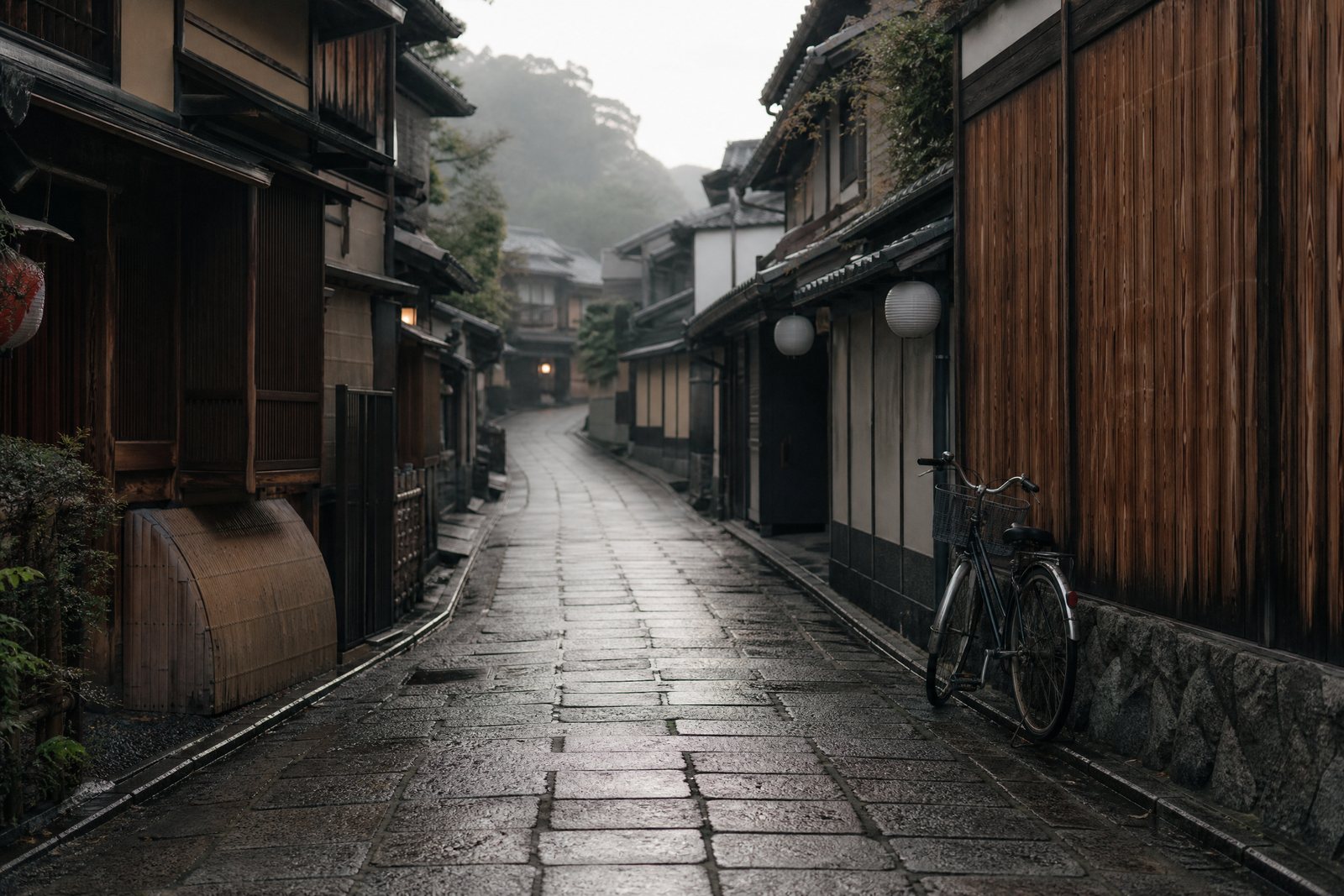 A rain-darkened stone lane between traditional wooden machiya homes in Kyoto